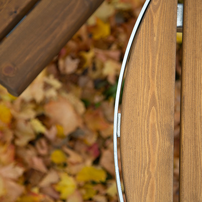 Close up shot of outdoor park furniture, you can see the detail in the wood, with autumn leaves fallen on the floor.